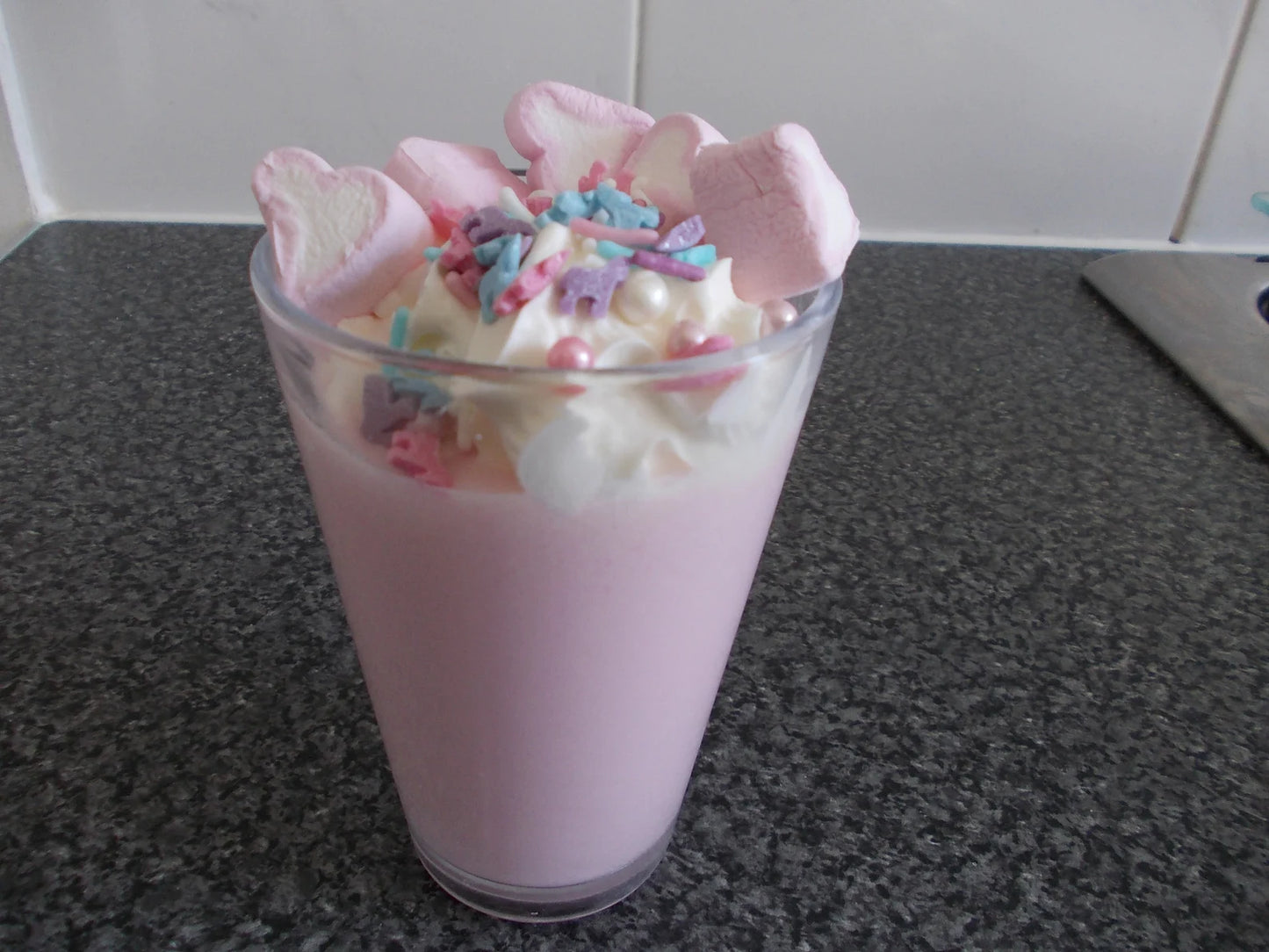 glass of pink unicorn milkshake toped with cream pink hart marshmallows and unicorn sprinkle